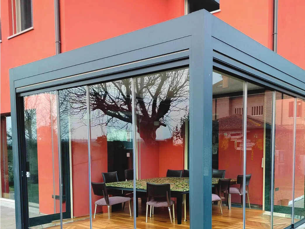 Grey pergola enclosed with Sliding Floor in front of a red house, with the dining table inside